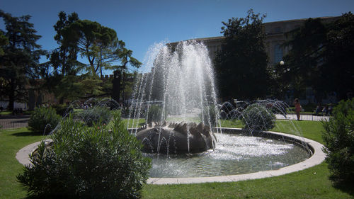 Water splashing fountain against trees and clear sky