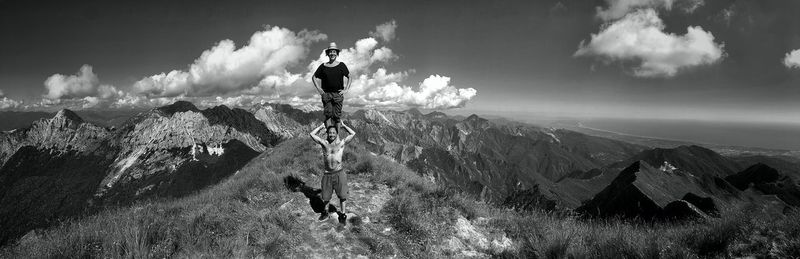 Woman standing on man shoulders over mountain against sky