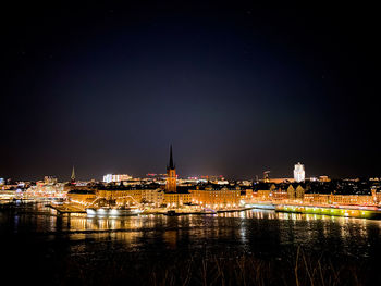 Illuminated buildings by river against sky at night