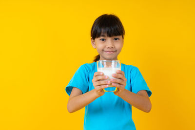 Portrait of smiling boy holding drink against yellow background