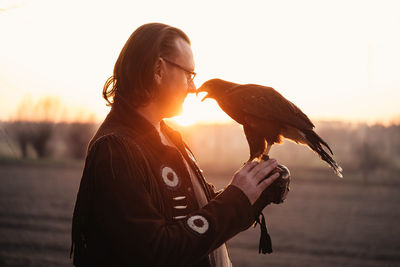 Man and wild bird over sunset sky looking on each other buzzard or eagle symbol of power, victory