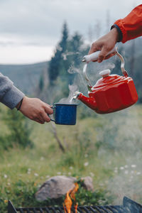 Pouring hot water from kettle into a coffee cup while camping in front of a campfire 