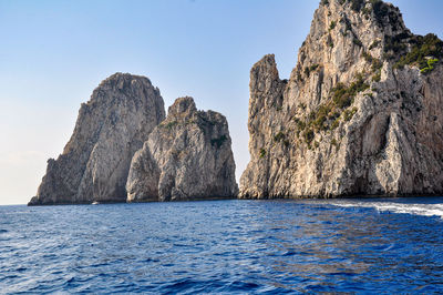 Rock formations in sea against clear blue sky