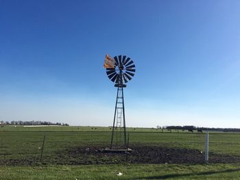 Windmill on grassy field against clear sky