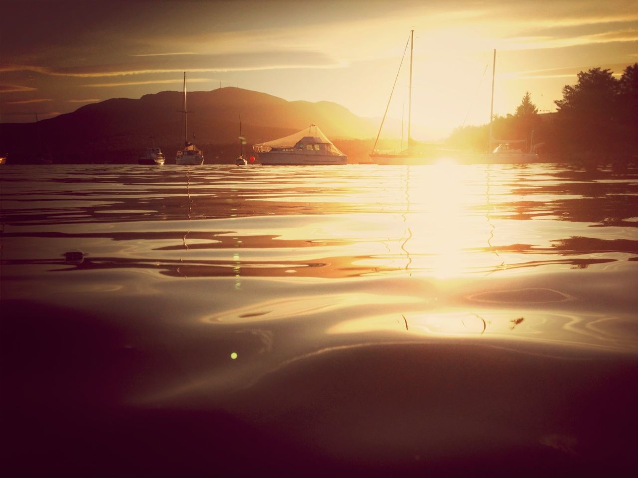 sunset, water, sun, reflection, mountain, sky, scenics, tranquility, tranquil scene, beauty in nature, lake, transportation, silhouette, sunlight, nautical vessel, nature, orange color, sunbeam, idyllic, boat