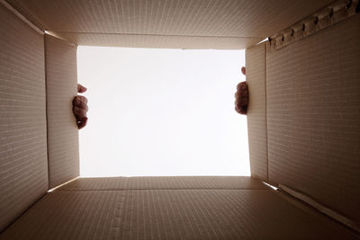 Cropped hands holding open cardboard box against white background