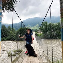 Portrait of woman with dog standing on footbridge over river