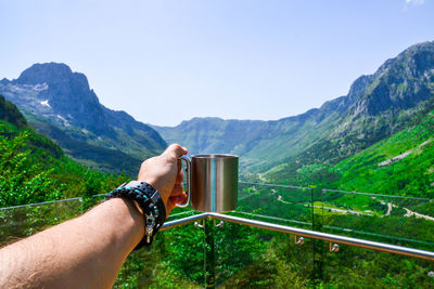 Man holding mug by mountain against clear sky
