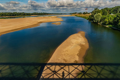 View of river valley with shadow of bridge against cloudy, blue sky.