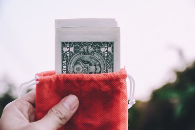 Cropped hand holding currency against sky