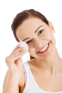 Close-up portrait of smiling young woman applying compact against white background