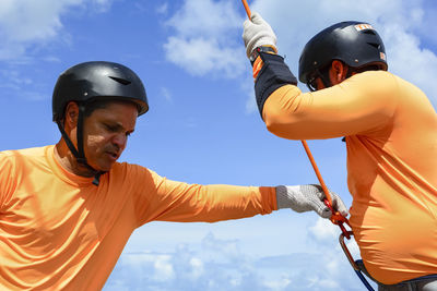 Low angle view of man holding rappel rope against sky