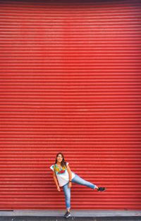 Full length portrait of woman standing against red shutter