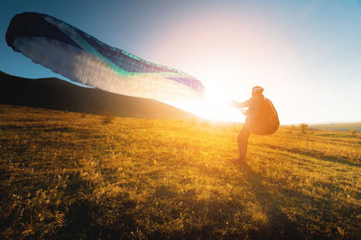 Paraglider with a blue parachute takes off. a male athlete stands on the field and lifts a