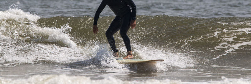 Front view of a man wearing a black wetsuit surfing at gilgo beach on long island.
