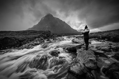 Rear view of woman standing by river against cloudy sky