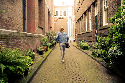 Rear view of woman walking on footpath amidst buildings