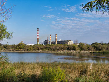 View of factory by lake against sky