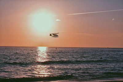 Seaplane flying over sea against sky during sunset