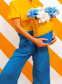 Unrecognizable woman on trend striped yellow background with flower arrangement in her hands. 