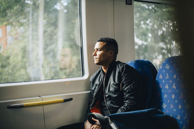 Thoughtful man looking through window while sitting in train