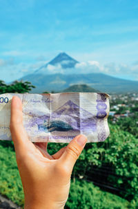 Cropped hand holding paper currency against mountain