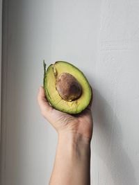 Cropped image of hand holding apple against wall