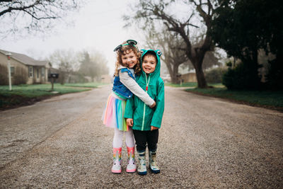 Young brother and sister standing outside hugging in rain