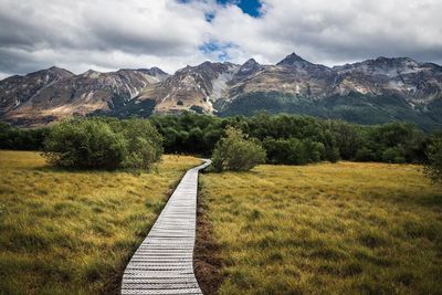 Boardwalk leading towards mountains against sky