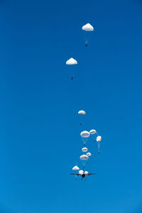 Low angle view of people with parachute against clear blue sky