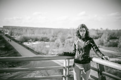 Portrait of young woman standing on bridge against sky