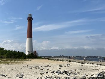 Lighthouse on beach by buildings against sky