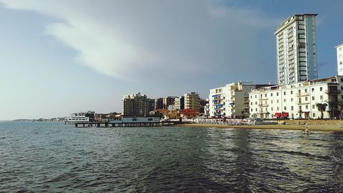 Sea by buildings against sky in city