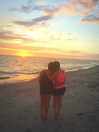 Rear view of couple standing on beach against sky during sunset