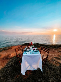 Chairs and table on beach against sky during sunset