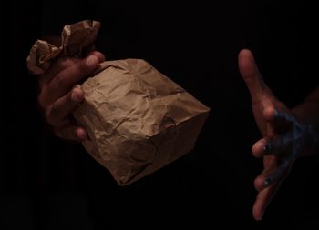Close-up of human hand holding paper bag against black background