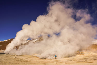 Man standing by geyser smoke against sky