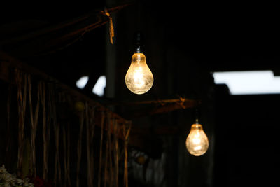 Low angle view of illuminated light bulb hanging from ceiling