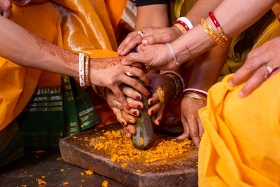 Midsection of women grounding turmeric on stone