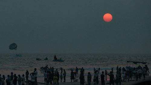 People at beach against clear sky during sunset
