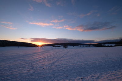 Scenic view of snow covered field against sky during sunset