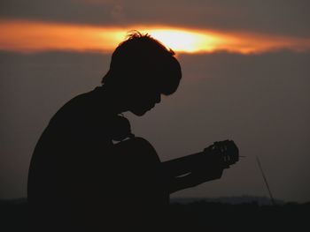 Silhouette man playing guitar against sky during sunset