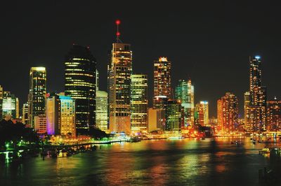 Illuminated buildings in front of river at night