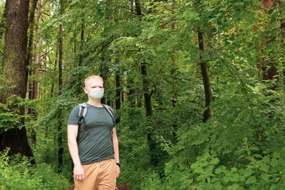 European young blond man in a disposable medical mask walks in the forest.