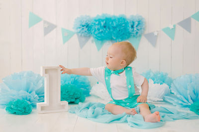 A beautiful one year old boy in turquoise clothing reaches for the number 1 in the photo zone 