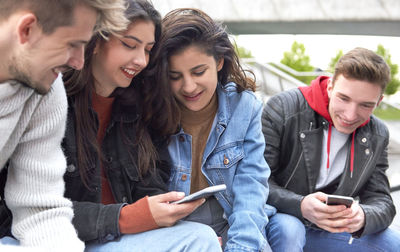 Friends using smart phone while sitting at park in city