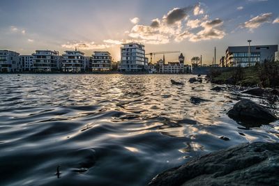 Sea by buildings against sky during sunset