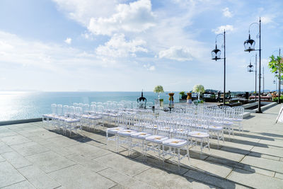 Empty chairs by sea against sky