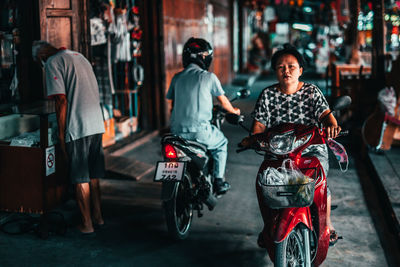 Rear view of people riding motorcycle on street in city