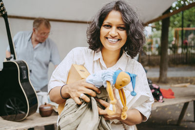 Portrait of happy woman holding books and stuffed toy at flea market